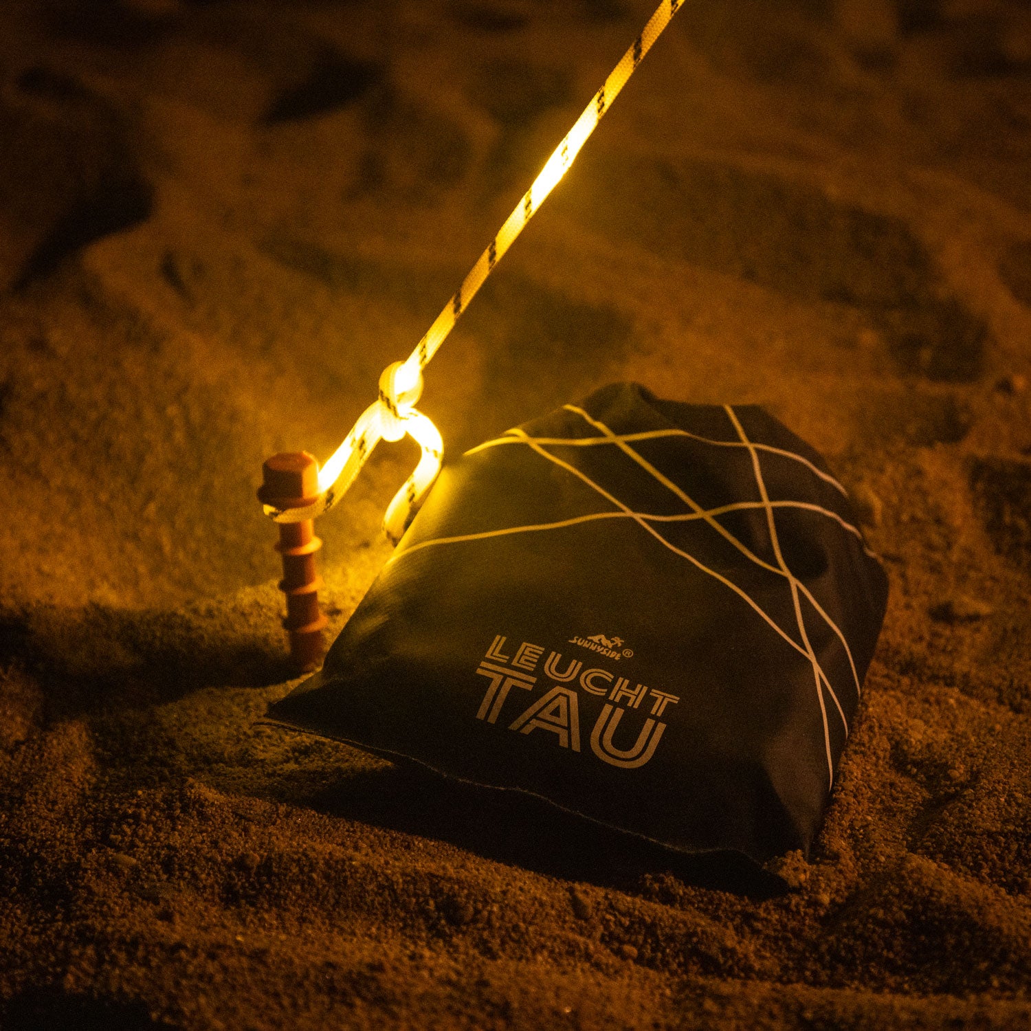 LEUCHTTAU Drybag liegt im Sand neben Peggy Peg Hering und LEUCHTTAU